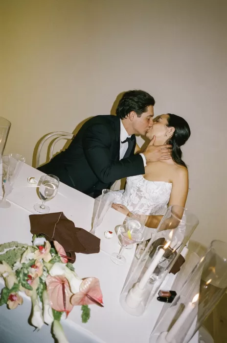 Bride and groom kiss at their reception table surrounded by candles and florals