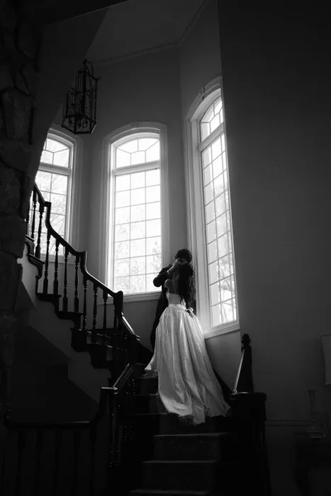 Black and white staircase portrait of the couple beneath soaring windows at Stone Haven.