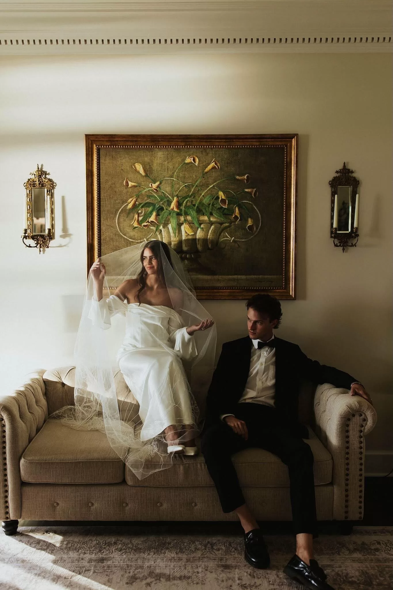 Bride sitting gracefully with veil draped over her, groom seated beside her on a sofa at Stone Haven.
