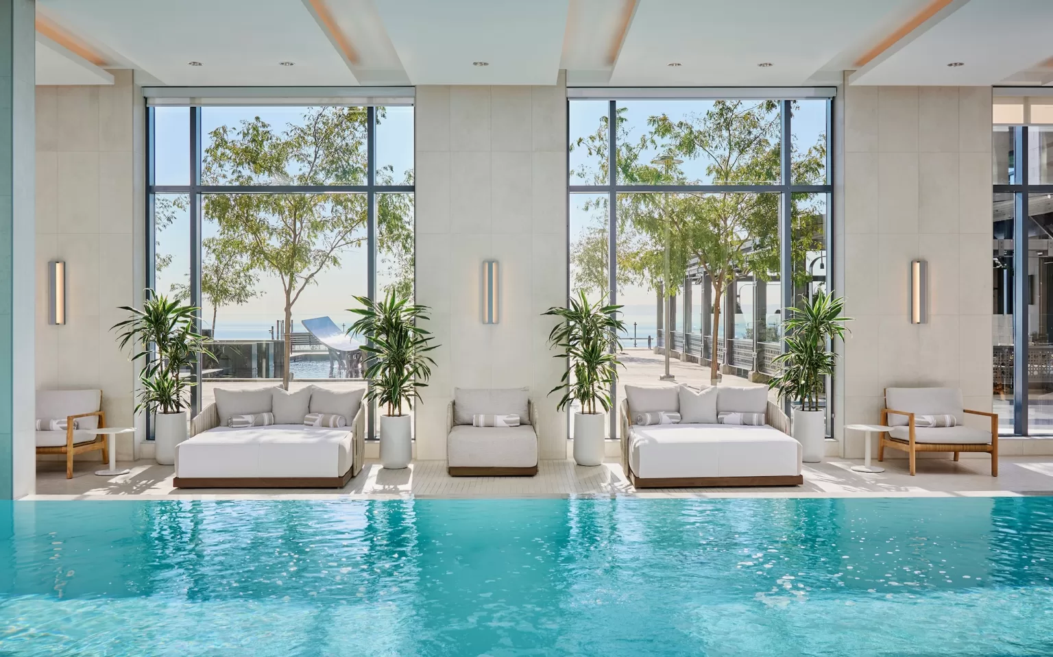 Indoor spa pool with loungers, tall windows and views toward the waterfront.
