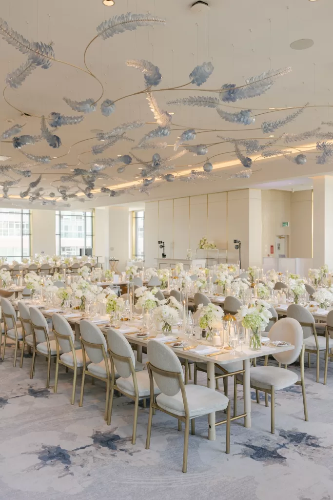 Wedding reception tables with white florals and sculptural pale blue ceiling decor.