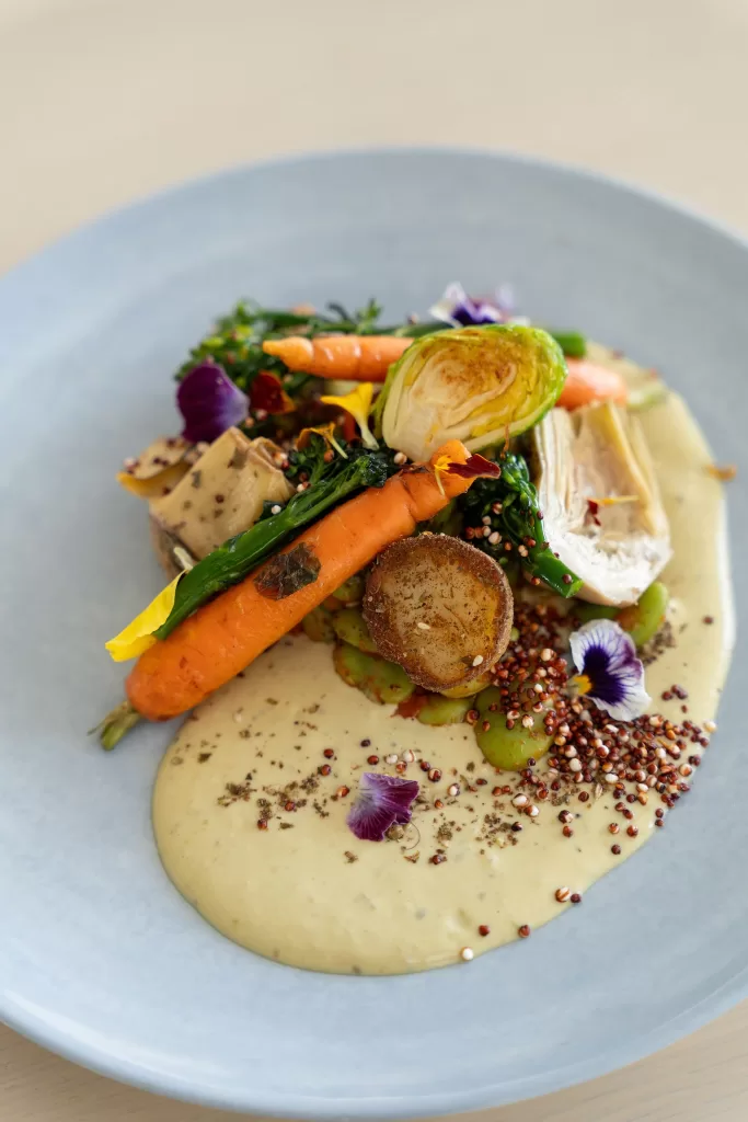 Colourful vegetable entrée with carrots, greens, quinoa and edible flowers.