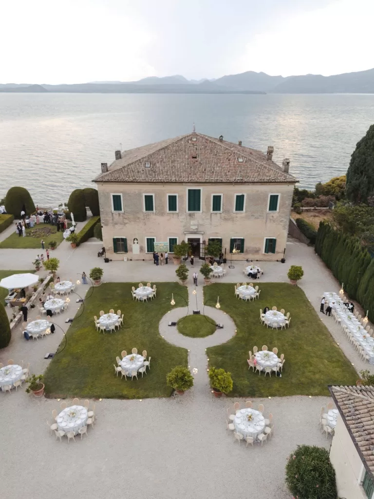 Aerial view of Villa San Vigilio's lakefront garden reception setup, surrounded by cypress trees and soft evening light.