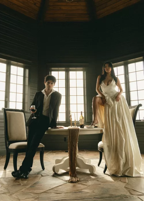 The couple pose with wine in a softly lit room with dark wood walls.