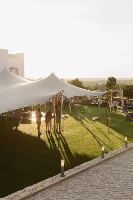 Guests mingling beneath a white stretch tent on a sunlit Algarve lawn.
