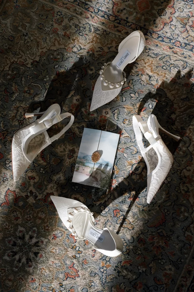 Lace bridal shoes and an illustrated invitation arranged across a patterned rug.