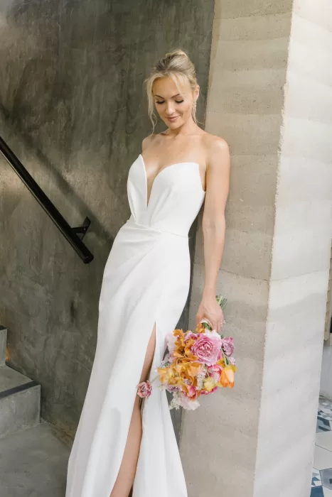 Close portrait of the bride with a pink and orange bouquet beside textured concrete.