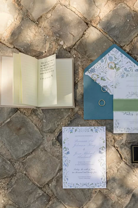 Wedding stationery, rings, and a handwritten note styled on stone paving.