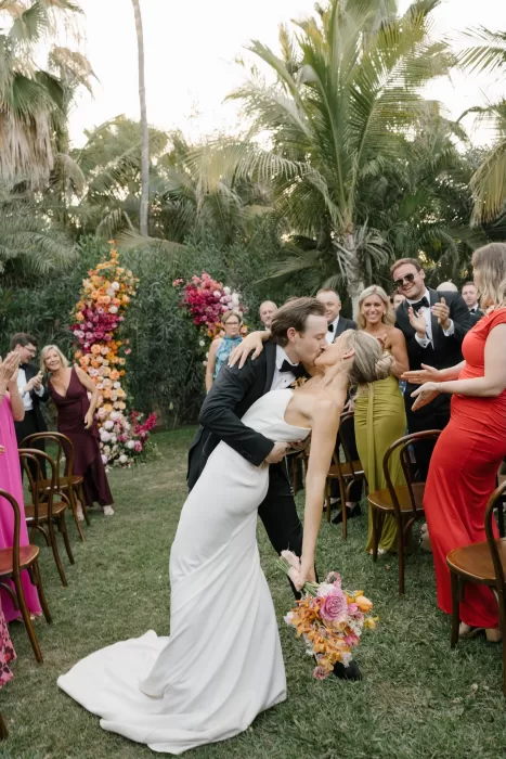 Newlyweds kissing in the garden aisle as guests cheer around them.