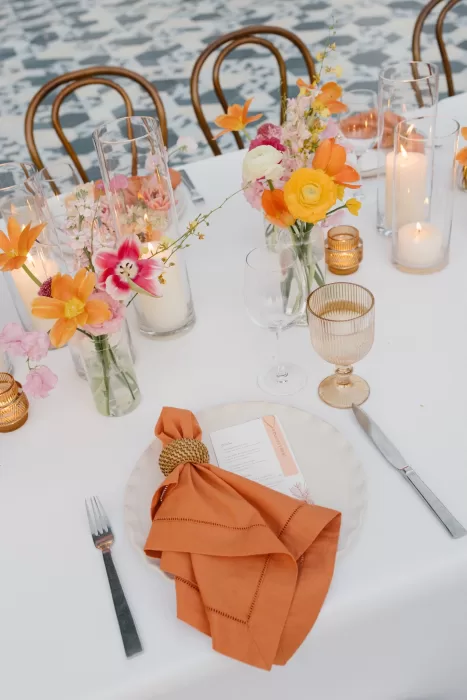 Coral napkin, candlelight, and bright flowers arranged across a refined reception table.