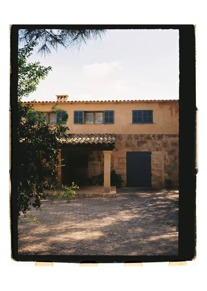 Rustic finca façade with blue shutters and shaded entrance, framed by surrounding greenery
