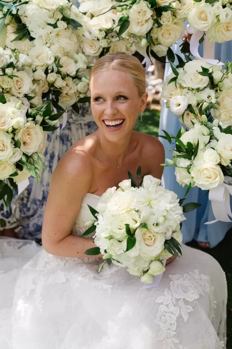 Bride smiling with an ivory rose bouquet surrounded by soft white florals.