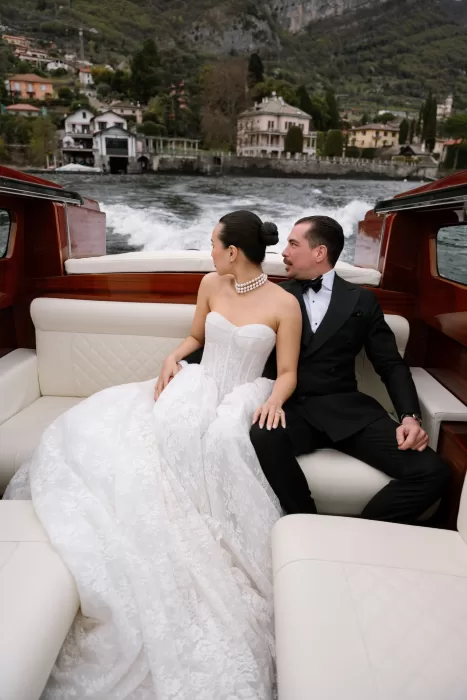 Couple seated on a polished wooden boat as the Lake Como shoreline slips behind them.