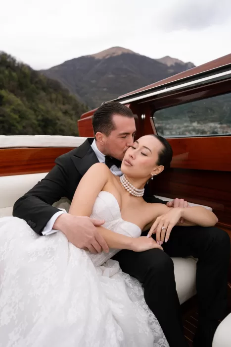 Groom kissing the bride’s forehead on a wooden boat beneath the mountain skyline.