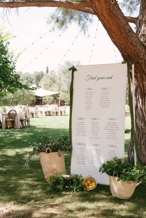 Elegant wedding seating chart displayed under a tree in a Mallorca finca garden with natural decor