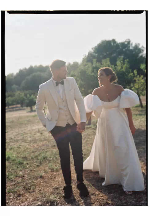 Bride and groom walking hand in hand through fields, glowing in golden hour light