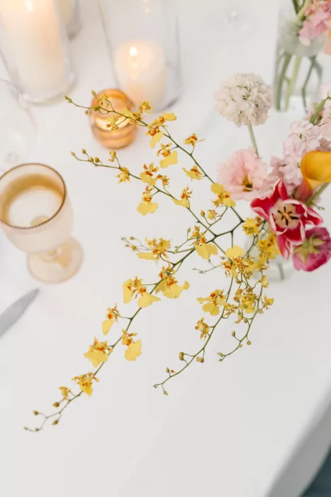 Yellow orchids and soft pink flowers arranged with candlelight on a white table.