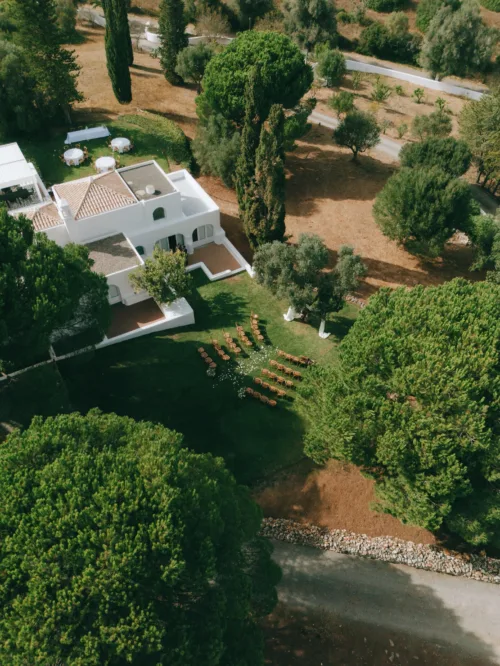 An aerial view shows the villa grounds, ceremony chairs and surrounding trees from above.