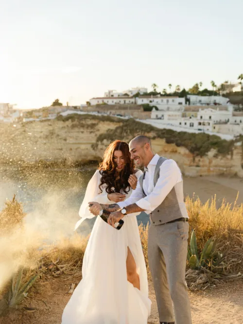 Bride and groom opening champagne on the Algarve cliffs at sunset after their wedding ceremony