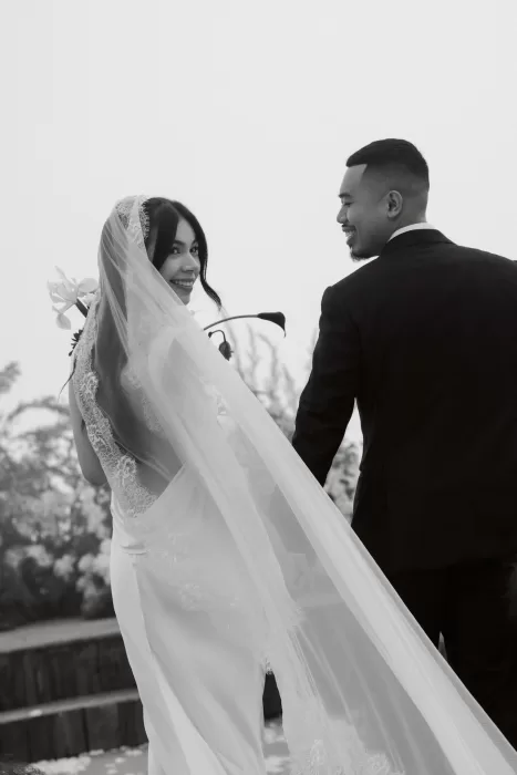 A black-and-white portrait of the couple smiling together beneath the bride’s lace veil.