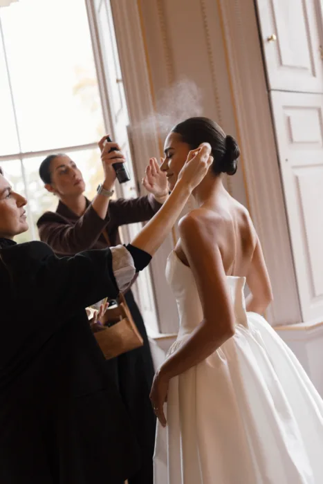 Makeup artist applying finishing touches to the bride before the wedding ceremony
