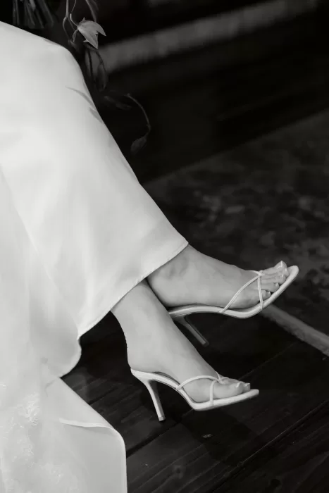 A black-and-white detail of the bride’s white strappy heels beneath her dress.