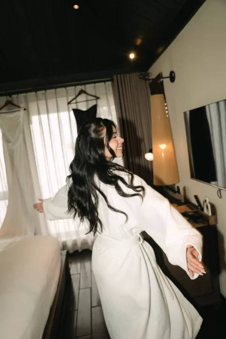 The bride smiles in a white robe inside the suite before getting dressed.