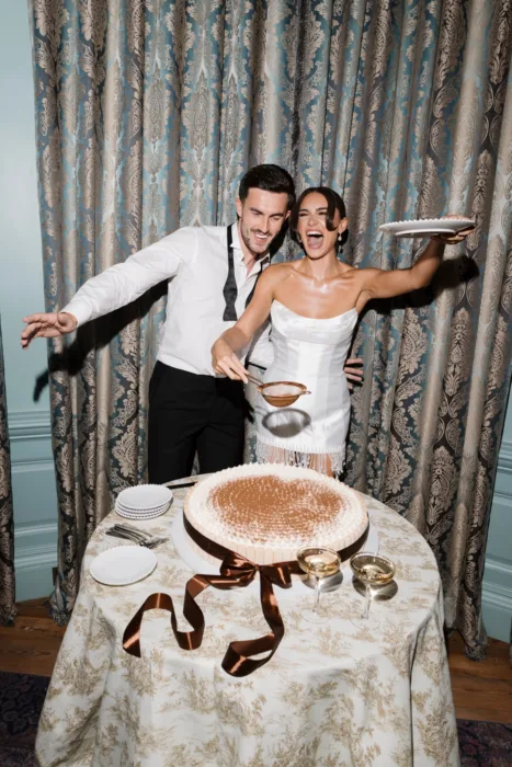Bride and groom celebrating as they finish decorating their wedding cake with cocoa powder
