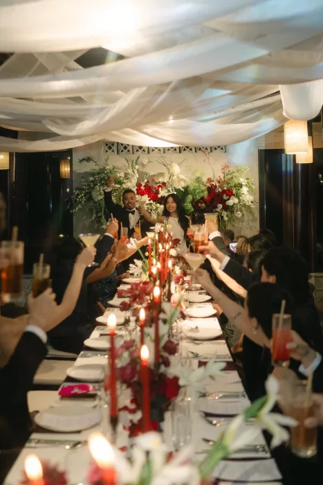 Guests toast the couple across a long candlelit table beneath softly draped fabric.