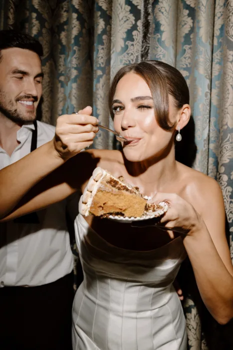 Groom feeding the bride a slice of wedding cake during the evening celebration