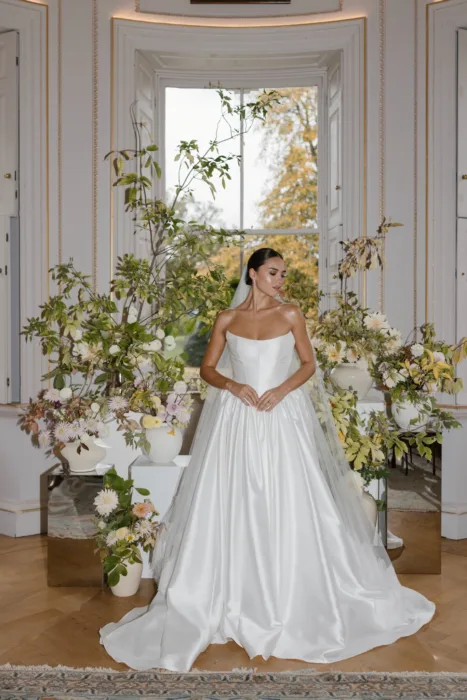 Bride posing beside abundant seasonal floral arrangements inside a country house