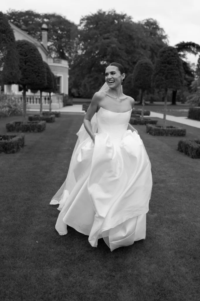 Bride walking through formal gardens with her satin wedding gown gathered in her hands