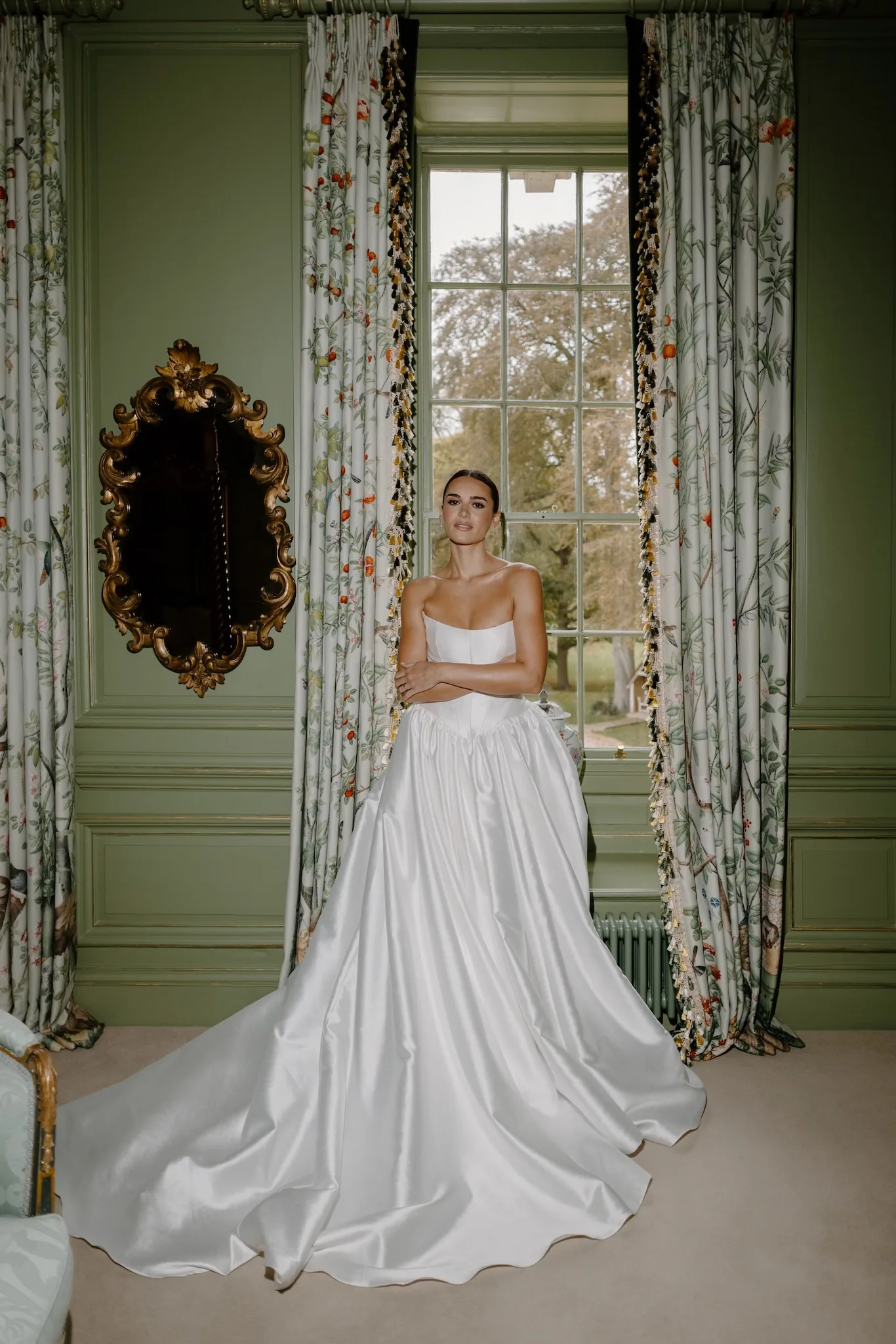 Bride standing in a green-panelled bridal suite wearing a satin wedding gown