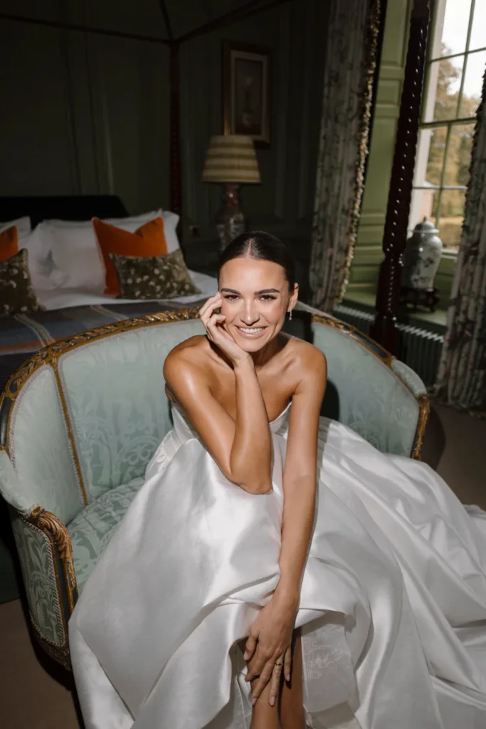 Bride smiling while seated on an antique sofa inside the bridal suite at Hotham Hall
