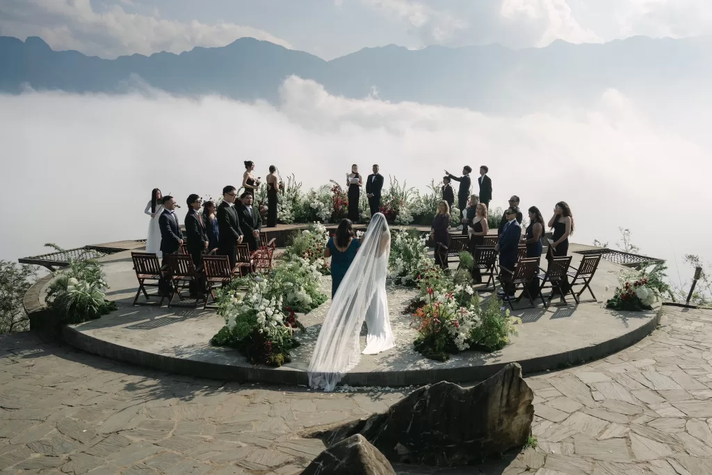 The bride walks toward the ceremony platform as guests stand above the clouds.