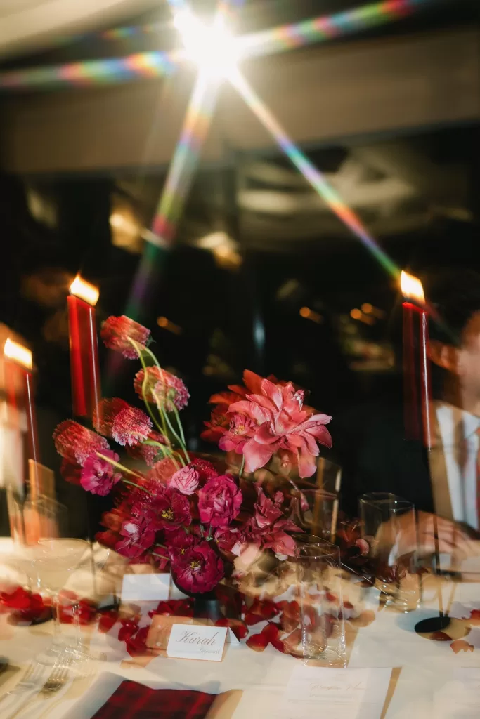 Red candles and vivid flowers glow across the reception table in warm evening light.