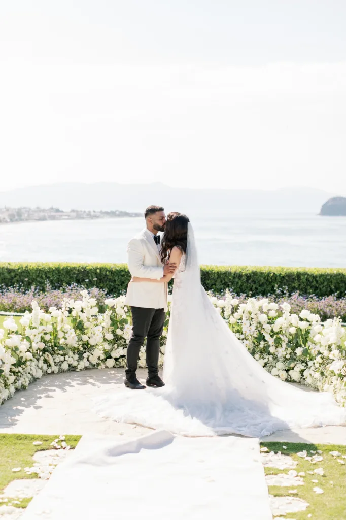 Bride and groom kiss at the floral ceremony space overlooking the water.
