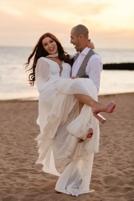 Groom carrying the bride along the beach at sunset after their Algarve wedding