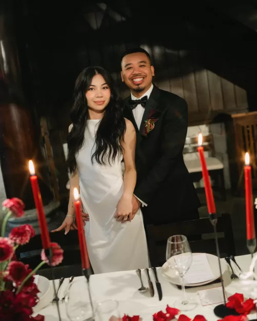 The couple pose beside red taper candles during their intimate Villa de Mont reception.