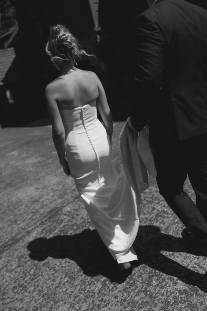 Black and white image of the bride walking in bright sun beside the groom.