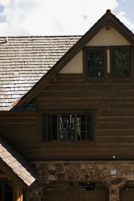 Rustic timber lodge exterior with stonework, shingle roof and forest reflected in the windows.