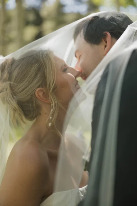 Close-up of the couple kissing beneath the bride’s veil in soft outdoor light.