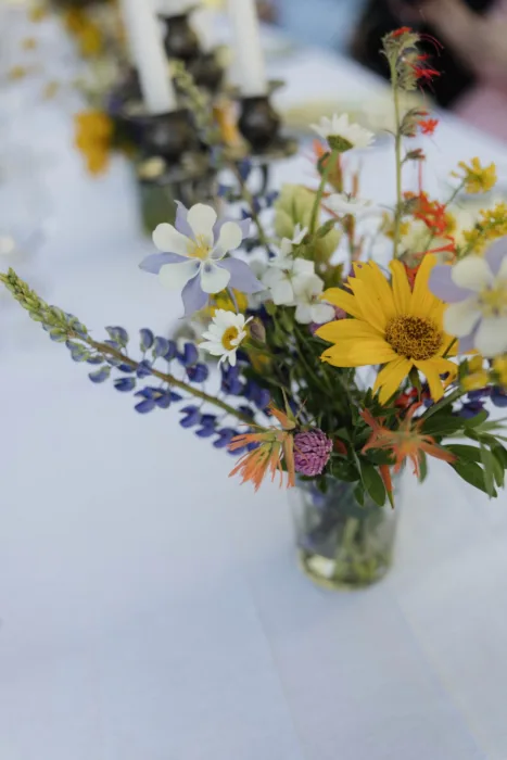 Colourful wildflower arrangement with daisies, lupins and candles on a wedding table.